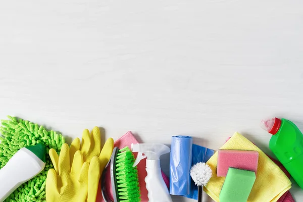 Bottles of detergent and cleaning tools on white wooden background top view. Housework cleaning concept. Copy space.