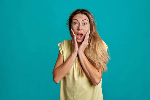 Retrato de estudio de una joven guapa de pelo rubio. Emociones de una chica sobre un fondo azul . — Foto de Stock