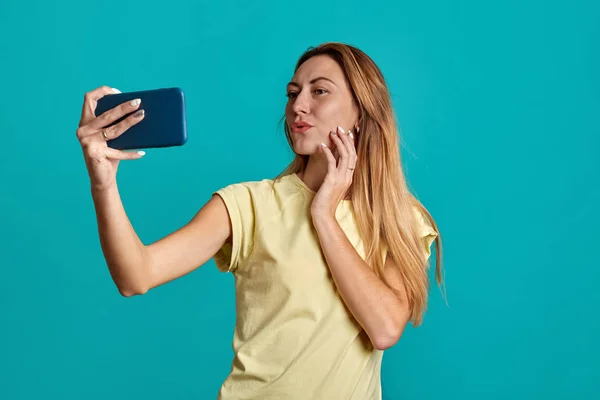 Beautiful girl portrait with half length phones on a blue background. A young woman takes a selfie and speaks on the phone. — Stock Photo, Image