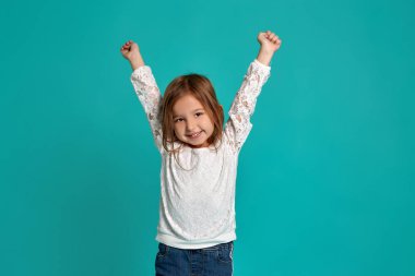 Mavi arka planda beyaz kazaklı küçük bir kız. Bir çocuğun duyguları işte. Küçük güzel bir kızın yakın çekim stüdyosu..