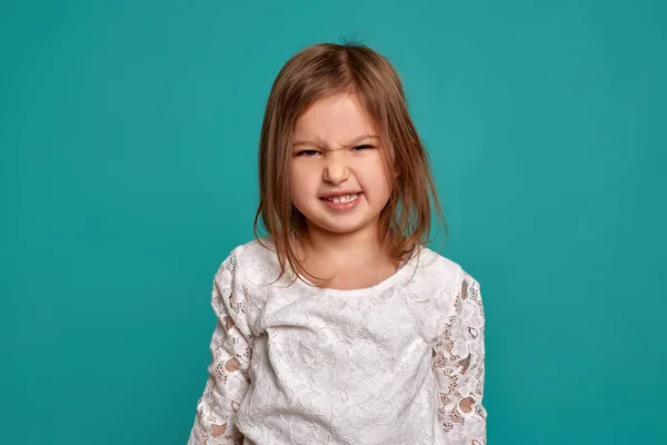 Niña con un suéter blanco sobre fondo azul. Emociones de un niño. Primer plano del estudio de una hermosa niña . — Foto de Stock