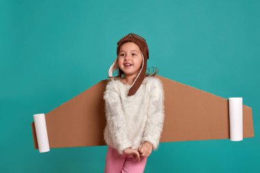 Küçük kız mavi arka planda oyuncak kanatlarla oynuyor. Astronot kostümü giymiş mutlu bir çocuk astronot olma hayalleri kurar. Bir çocuğun portresi.