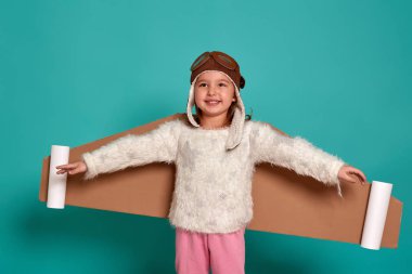 Küçük kız mavi arka planda oyuncak kanatlarla oynuyor. Astronot kostümü giymiş mutlu bir çocuk astronot olma hayalleri kurar. Bir çocuğun portresi.