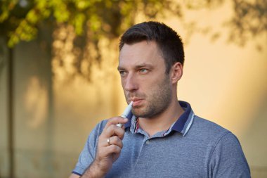 Elektronik sigara, sigara teknolojisi. Tütün Iqos sistemi. Isıtıcıyla elektrikli sigara içen bir adamın yakın çekimi. Yeni tütün ısıtma sistemi yakılmadan.