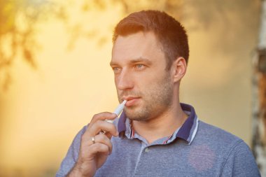 Elektronik sigara, sigara teknolojisi. Tütün Iqos sistemi. Isıtıcıyla elektrikli sigara içen bir adamın yakın çekimi. Yeni tütün ısıtma sistemi yakılmadan.