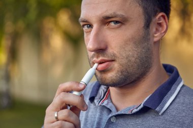 Elektronik sigara, sigara teknolojisi. Tütün Iqos sistemi. Isıtıcıyla elektrikli sigara içen bir adamın yakın çekimi. Yeni tütün ısıtma sistemi yakılmadan.