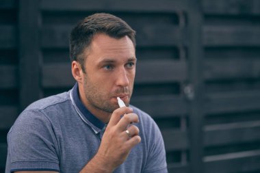 Elektronik sigara, sigara teknolojisi. Tütün Iqos sistemi. Isıtıcıyla elektrikli sigara içen bir adamın yakın çekimi. Yeni tütün ısıtıcısı yanıyor.