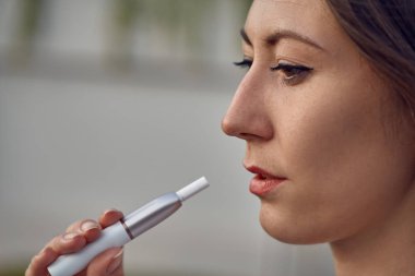 Elektronik Sigara Teknolojisi. Tütün Iqos sistemi. Isıtma yastığıyla elektrikli sigara içen bir kızın yakın çekimi. tütün ısıtma sistemi. Kadın ellerinde elektronik sigara..