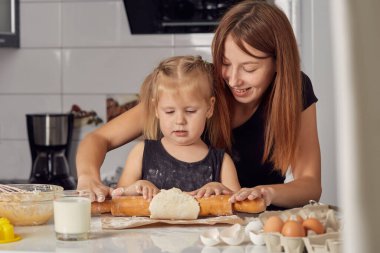 Anne ve kız, un, süt ve modern bir mutfaktaki bir masada oturarak tatlı bir pasta hazırlıyorlar. Elinde çırpı tutan, kasede yumurta karıştıran, annesiyle krep hamuru hazırlayan bir kız..