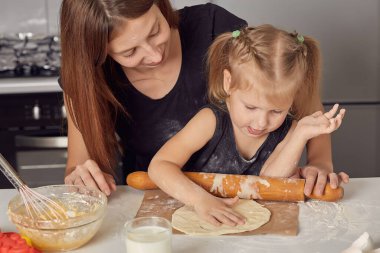 Anne ve kız, un, süt ve modern bir mutfaktaki bir masada oturarak tatlı bir pasta hazırlıyorlar. Elinde çırpı tutan, kasede yumurta karıştıran, annesiyle krep hamuru hazırlayan bir kız..