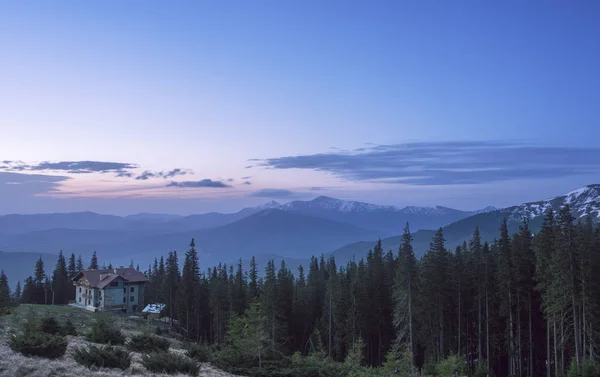 Casa en una colina de montaña al amanecer. Cabaña en un bosque con vista a una cordillera — Foto de Stock