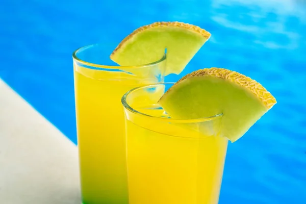 Glasögon med gul cocktail framför en pool med klart vatten. Makro foto av cocktails. — Stockfoto