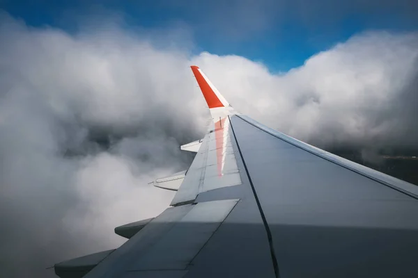 View at the airplane that leads for landing through white clouds. Blue sky is visible through clouds