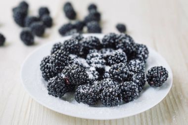 Olgun çilek böğürtlen ahşap bir masa üzerinde beyaz bir tablo. Sağlıklı kahvaltı hayati vitaminler ile. Pudra şekeri ile olgun böğürtlen.