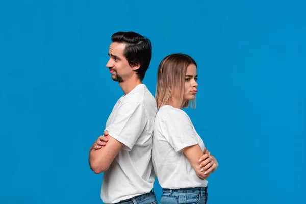 Couple bouleversé d'une jeune femme blonde et d'un homme barbu brunet avec moustaches en t-shirts blancs et jeans bleus posant isolés sur fond bleu . — Photo