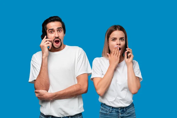 Blond žena a brunet muž v bílých tesáky a modré džíny jsou překvapeni mluvení po telefonu. — Stock fotografie