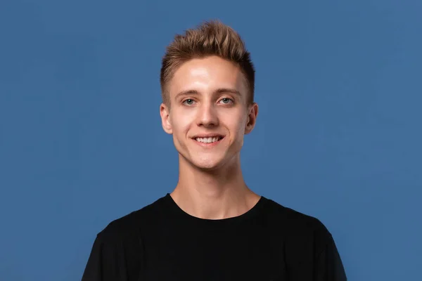 Close-uo retrato de um adolescente loiro sorridente em uma camiseta preta isolada sobre fundo azul . — Fotografia de Stock