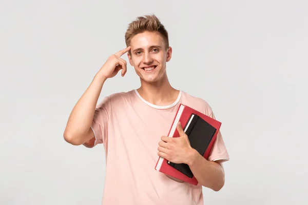 Jovem bonito em uma camiseta rosa com livros e arquivos apontando com o dedo na cabeça para expressar a ideia de pensar . — Fotografia de Stock