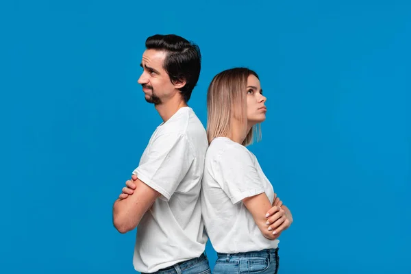 Couple bouleversé d'une jeune femme blonde et d'un homme barbu brunet avec moustaches en t-shirts blancs et jeans bleus posant isolés sur fond bleu . — Photo
