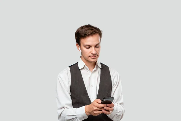 Joven hombre de negocios con camisa blanca y chaleco gris mirando a la pantalla de un smartphone . — Foto de Stock