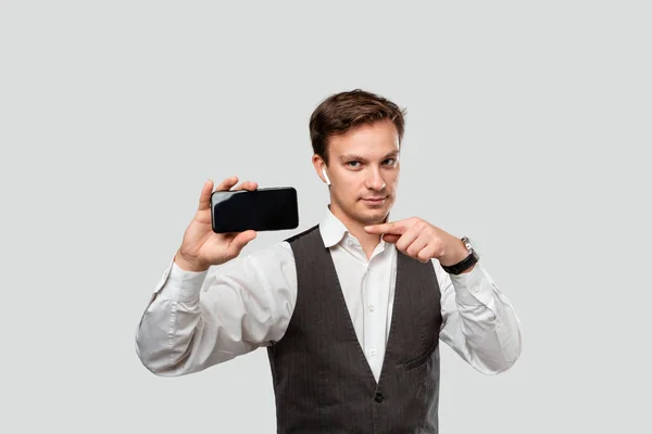 Hombre de negocios guapo en una camisa blanca y chaleco gris que muestra la pantalla de un teléfono inteligente . — Foto de Stock