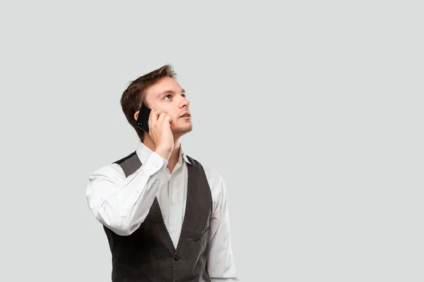 Joven hombre de negocios con camisa blanca y chaleco gris hablando en un smartphone . — Foto de Stock
