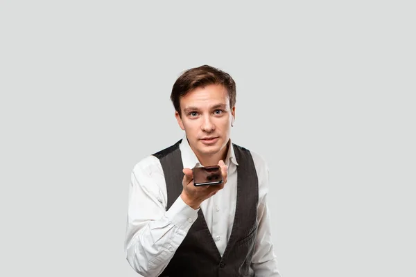 Joven hombre guapo en una camisa blanca y chaleco gris video chat en un teléfono móvil . — Foto de Stock