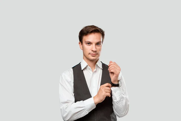 Joven hombre de negocios con camisa blanca y chaleco gris ajustando los relojes de mano mirando a la cámara . — Foto de Stock