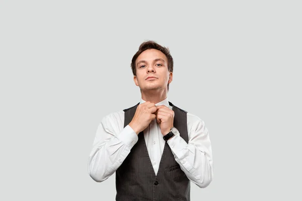 Jovem homem de negócios em uma camisa branca e colete cinza ajustando relógios de mão olhando para a câmera . — Fotografia de Stock