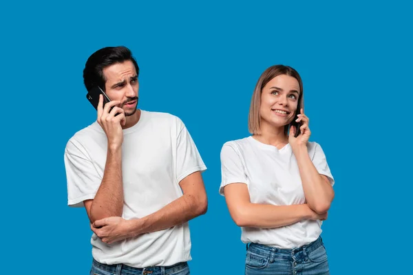 Eine blonde Frau und ein brünetter Mann in weißen T-Shirts und blauen Jeans unterhalten sich am Telefon.. — Stockfoto