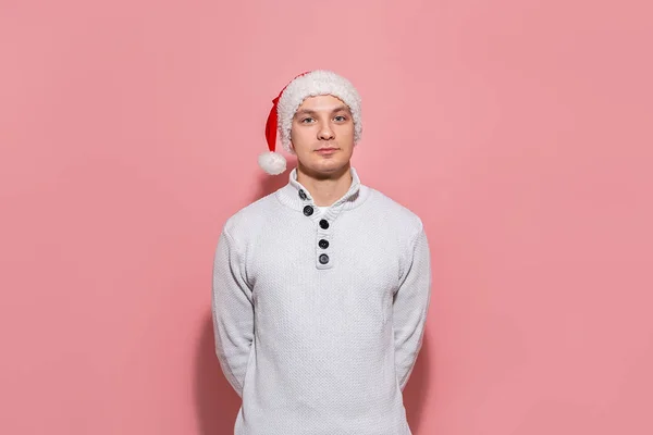 Bonito homem em um suéter branco e chapéu de Papai Noel isolado sobre fundo rosa . — Fotografia de Stock