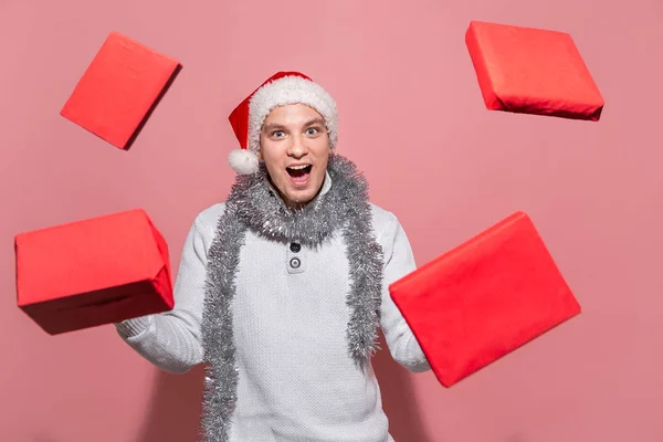 Homem bonito em uma camisola branca, chapéu de Papai Noel e trumpery mostra presentes de Natal mágicos levitando em torno dele . — Fotografia de Stock