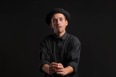 Tarz sahibi yakışıklı bir adam. Siyah arka planda siyah bir gömlek ve domuz pastası şapkası. Gösterişsiz bir portre.