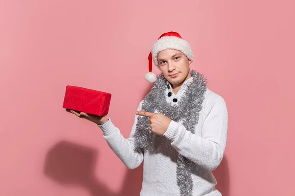 Homem de camisola branca e chapéu vermelho de Papai Noel segurando presentes de Natal em caixas vermelhas isoladas em fundo rosa . — Fotografia de Stock