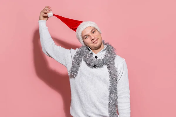 Hombre guapo en un suéter blanco quitándose el sombrero rojo de Santa . — Foto de Stock