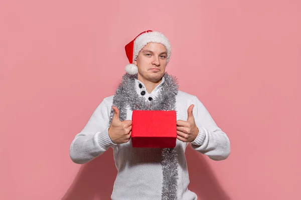 Homem de camisola branca e chapéu vermelho de Papai Noel segurando presentes de Natal em caixas vermelhas isoladas em fundo rosa . — Fotografia de Stock