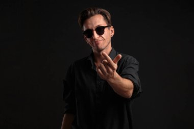 Siyah gömlekli ve güneş gözlüklü seksi adam parmaklarıyla cezbedici ve davetkar..