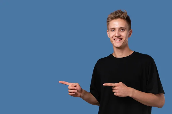 Jovem bonito em um tee preto apontando para o espaço vazio para publicidade . — Fotografia de Stock