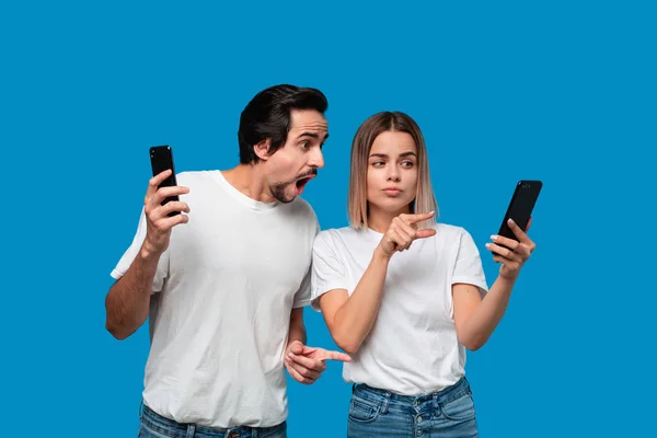 Homme en tee-shirts blancs et jeans bleus est choqué en regardant l'écran du smartphone d'une femme blonde . — Photo