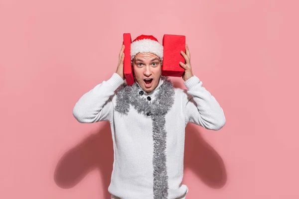 Man in een witte trui en rode Kerstman hoed is moe om kerstcadeaus te kiezen. — Stockfoto