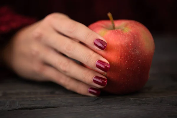 Nahaufnahme Foto einer Frau mit rotem Apfel in der Hand über schwarzem Holztisch. — Stockfoto