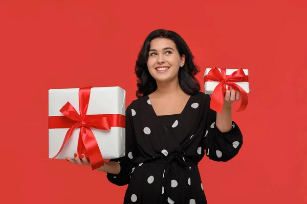 빨간 리본이 달린 작고 큰 크리스마스 경품 상자 사이를 선택하는 검은 드레스를 입은 아름다운 여인 — 스톡 사진
