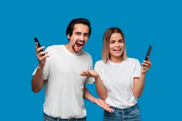 Femme et homme en tee-shirts blancs et jeans bleus sont surpris tenant smartphones regardant la caméra — Photo