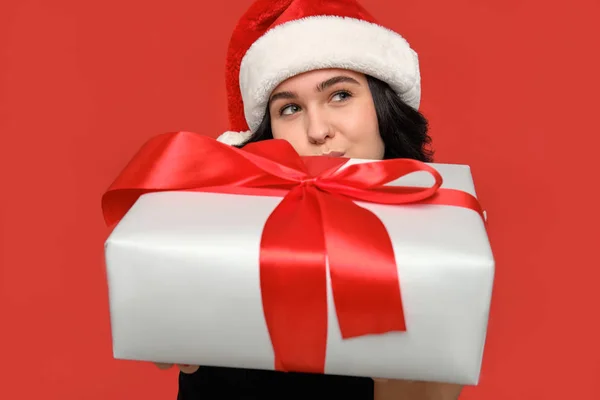 Kobieta w czarnej sukience i kapelusz Mikołaja ukrywa się za świątecznym pudełkiem białego koloru z czerwoną wstążką. — Zdjęcie stockowe