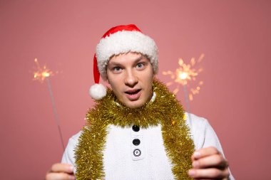 Bengal ışıkları tutan beyaz kazaklı ve kırmızı şapkalı heyecanlı bir adam.