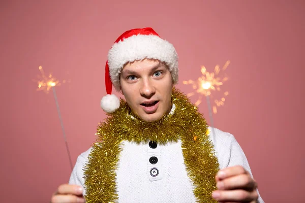 Homem excitado com uma camisola branca e chapéu vermelho de Papai Noel segurando luzes de Bengala — Fotografia de Stock