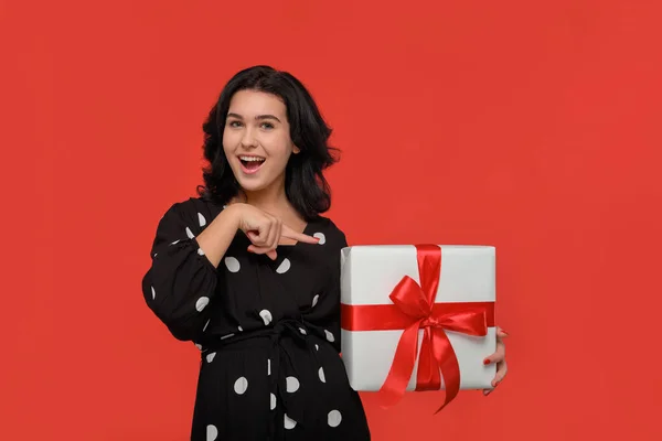 Bruneta žena v černých šatech s úsměvem drží vánoční dárkové krabice bílé barvy s červenou stuhou. — Stock fotografie