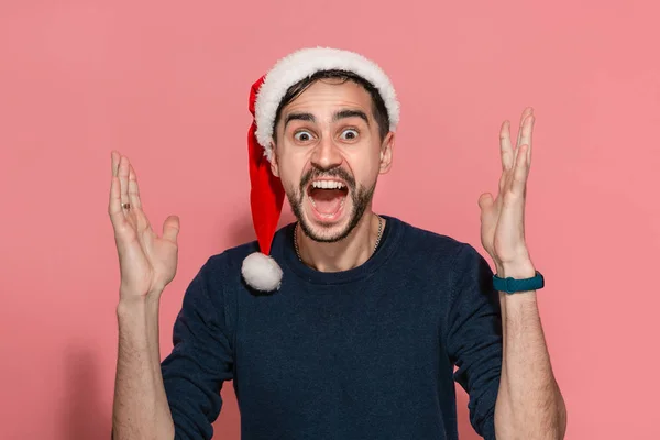 Az ember kék pulóverben és piros Mikulás sapkában nagyon izgatott, hogy megünnepelje a karácsonyt és az új évet.. — Stock Fotó