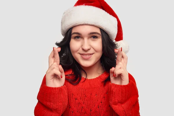 Mädchen in rotem Pullover und Weihnachtsmann-Hut, die Daumen drücken und vom besten Geschenk träumen — Stockfoto