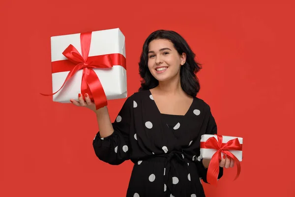 Mujer sonriente en un vestido negro elegir entre pequeñas y grandes cajas de regalo de Navidad con cinta roja — Foto de Stock